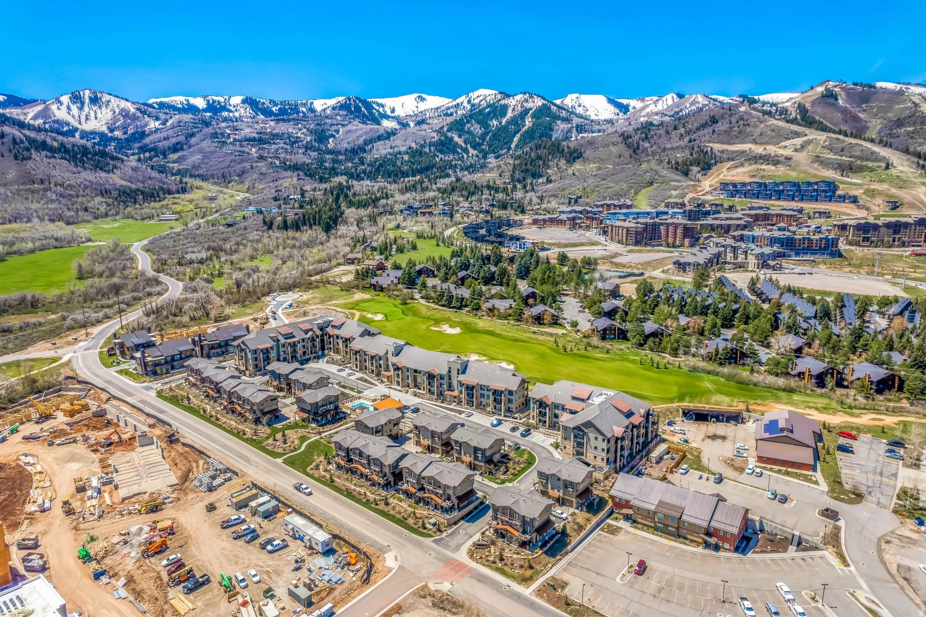 Aerial panorama featuring a residential community with multi-story buildings and townhomes, surrounded by mountainous terrain