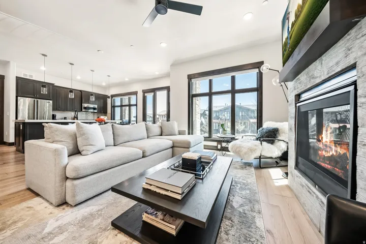Open-concept living area with light wood-finish flooring, a contemporary fireplace with a stone-finish surround, and a ceiling fan