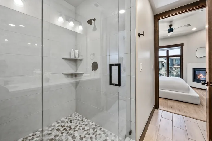 Glass-enclosed shower featuring large format tile walls and a pebble-style floor