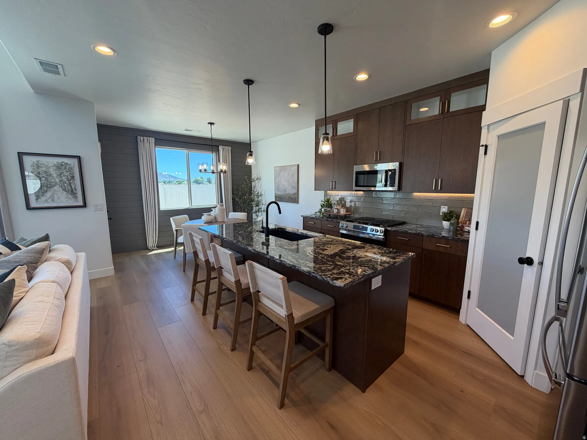 Open-concept kitchen and dining area featuring a large island with a granite countertop, stainless steel appliances, dark wood-finish cabinetry, and wood-finish flooring