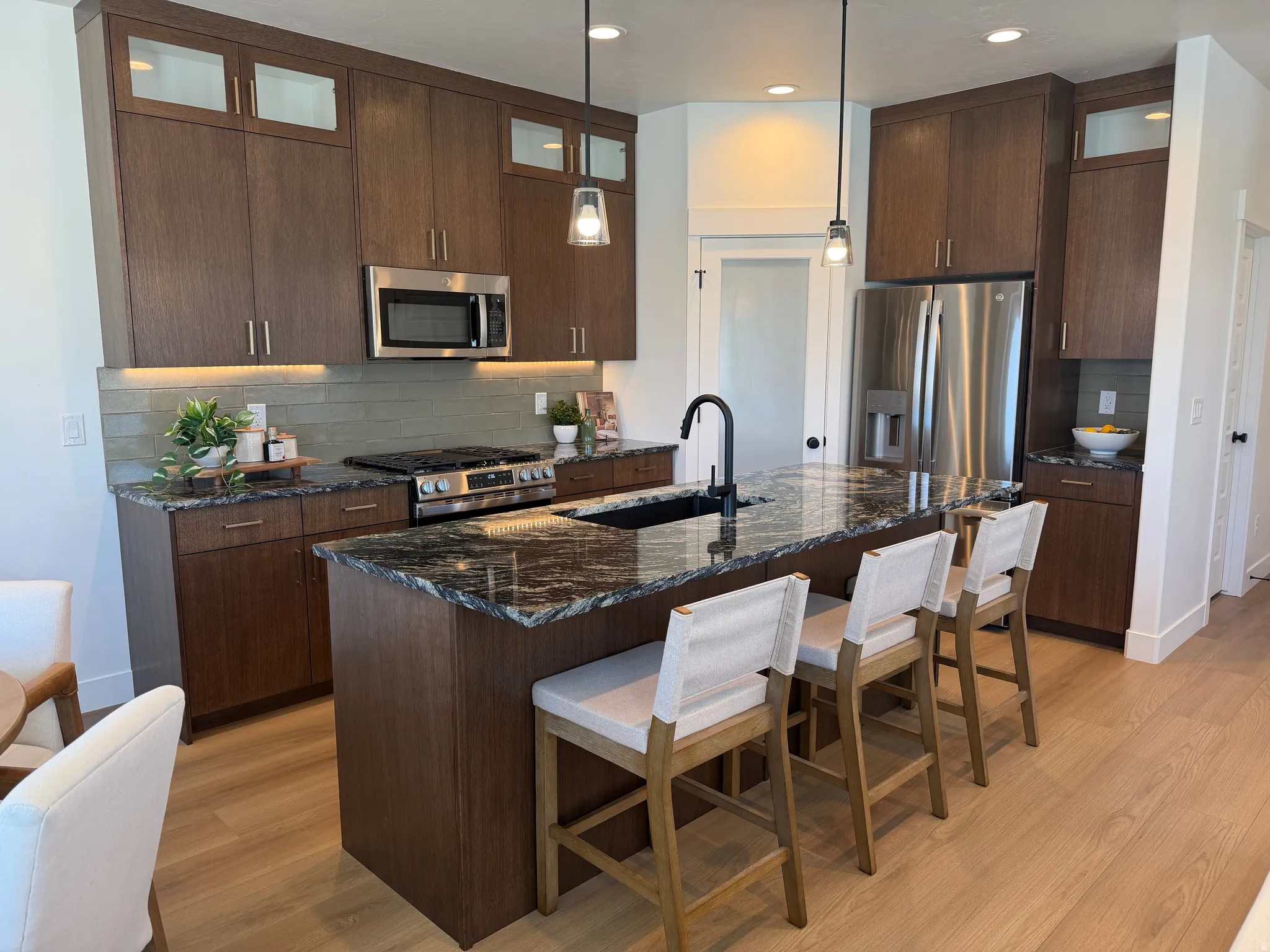 Contemporary kitchen featuring dark wood-finish cabinetry, a large kitchen island with a dark granite-style countertop, and light wood-finish flooring
