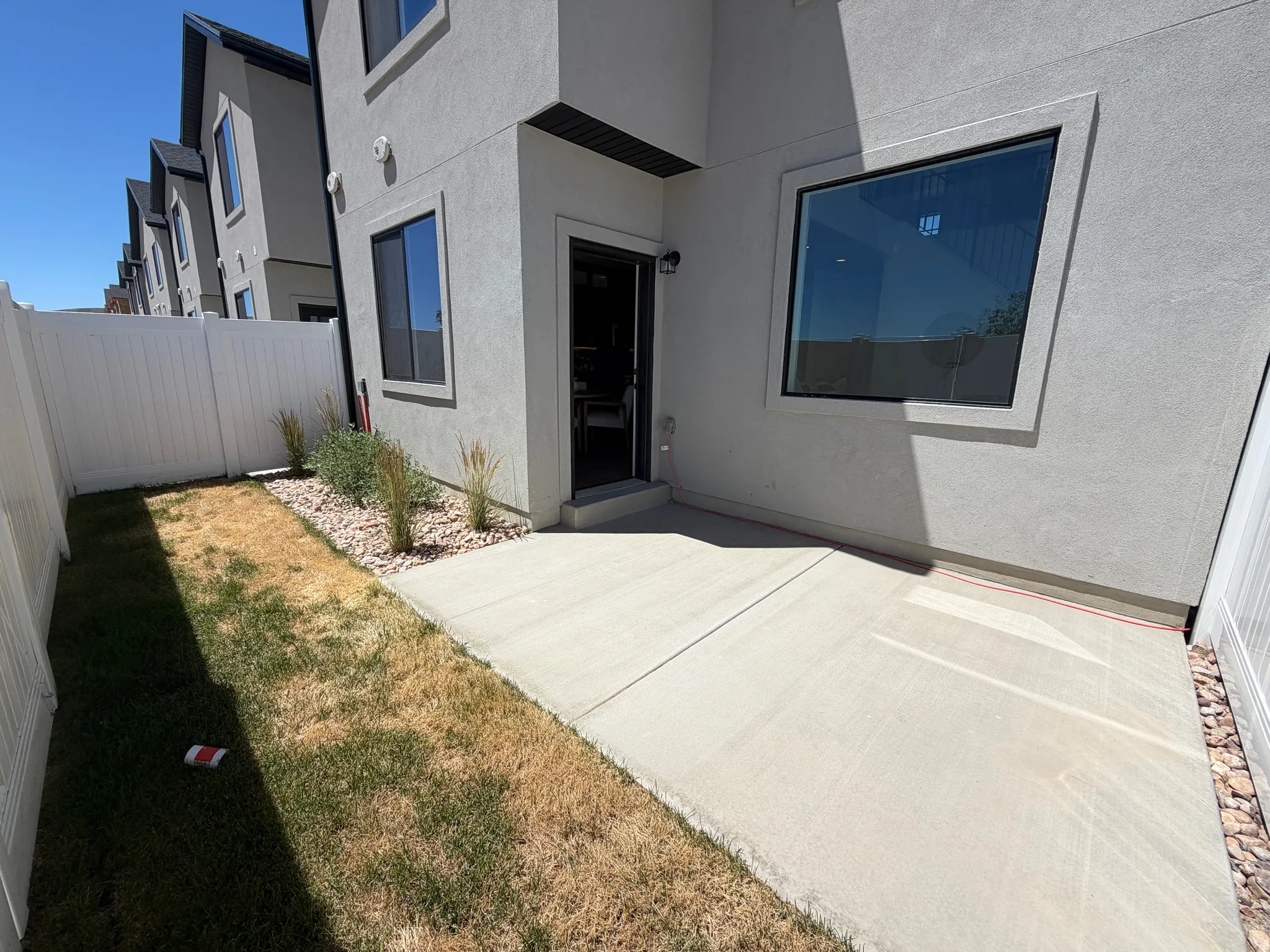 Rear patio space featuring a concrete slab, privacy fencing, and a landscaped rock bed with plantings