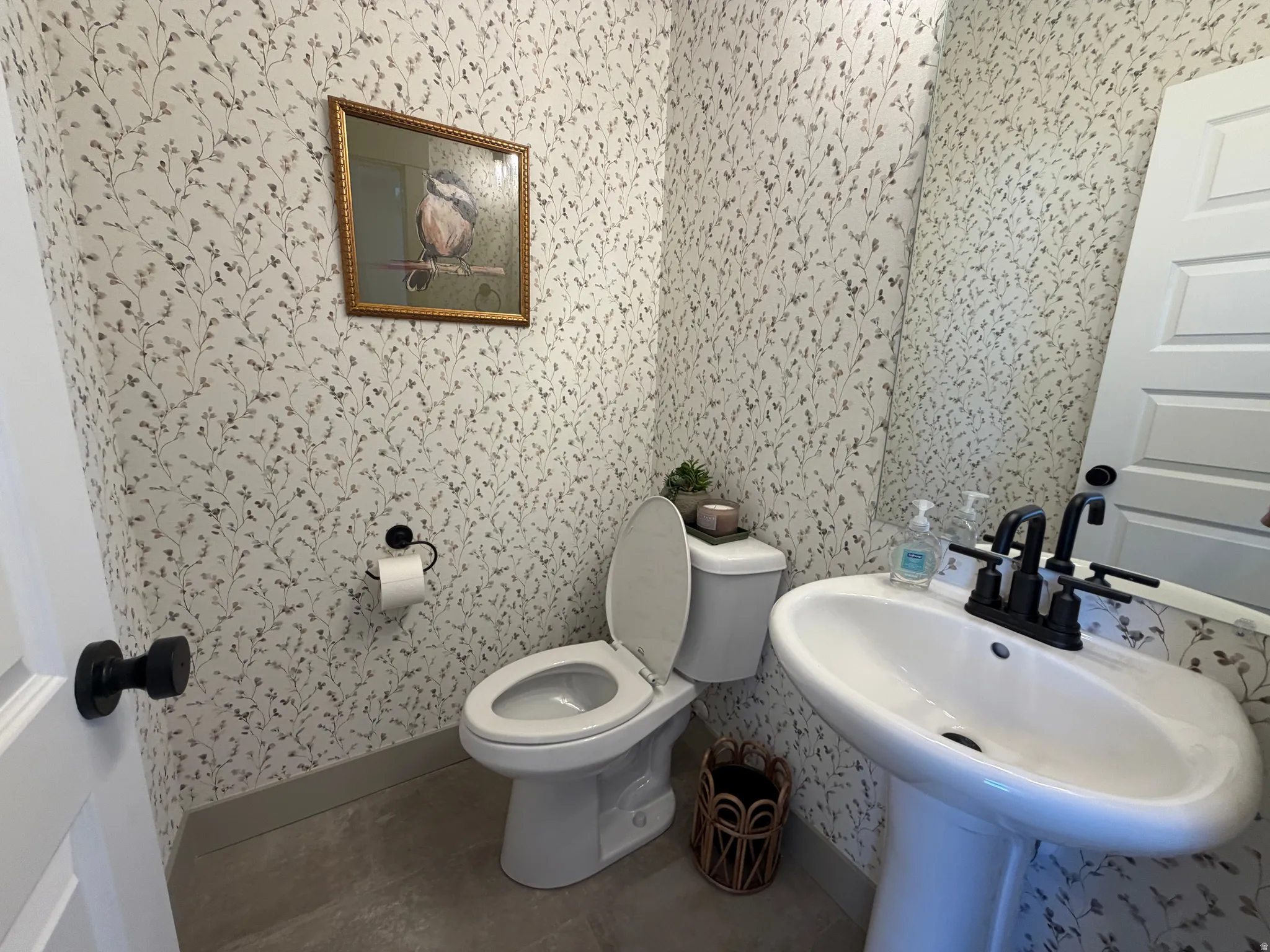 Powder room featuring a pedestal sink with matte black fixtures, botanical wallpaper, and durable flooring