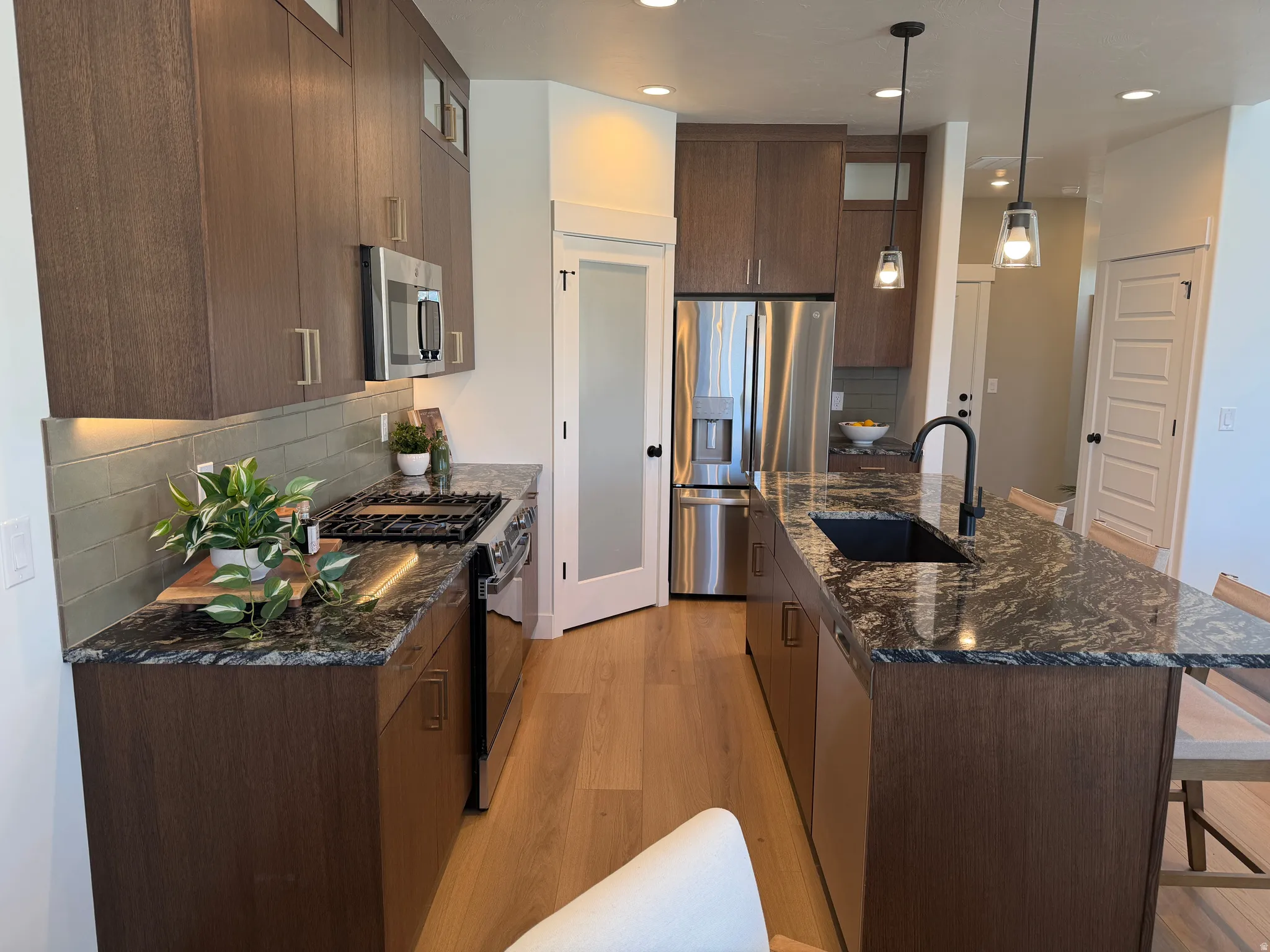 Gourmet kitchen featuring dark wood-finish cabinetry, stainless steel appliances, speckled stone countertops, and wood-finish flooring