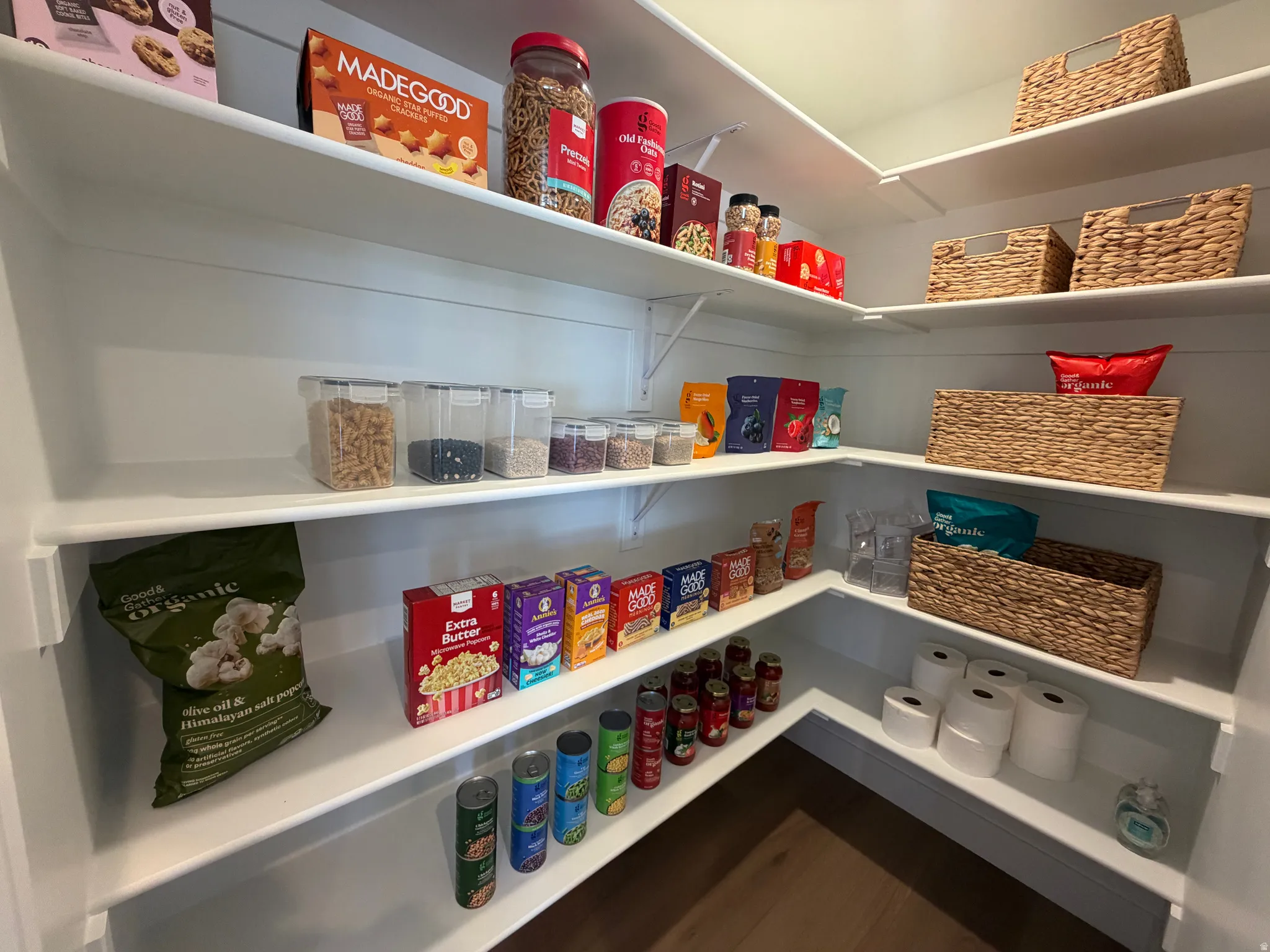 Walk-in pantry with extensive white shelving, L-shaped configuration, light wood-finish flooring, and ample storage capacity
