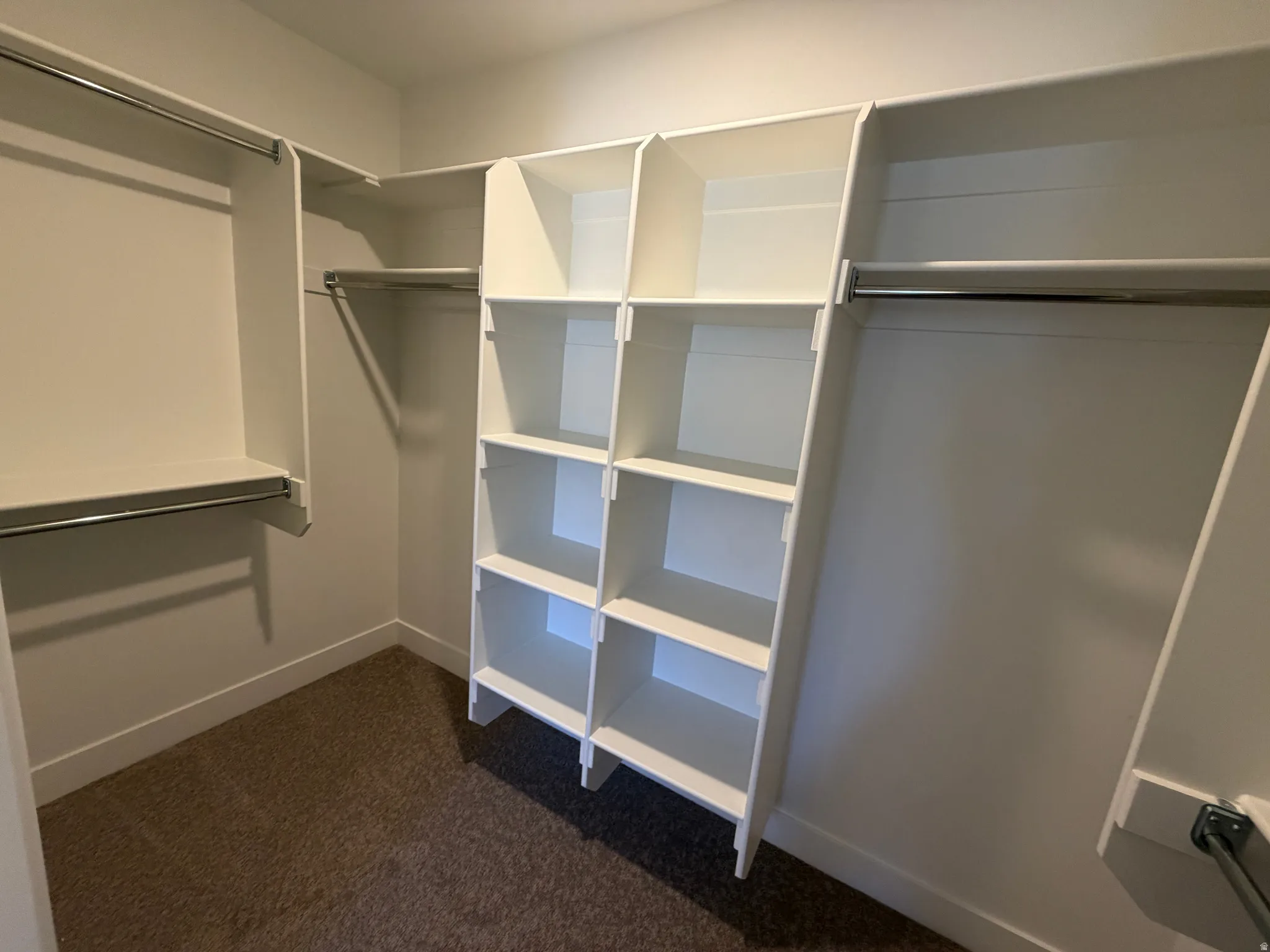 Walk-in closet featuring built-in white shelving, multiple hanging rods, and brown carpet flooring