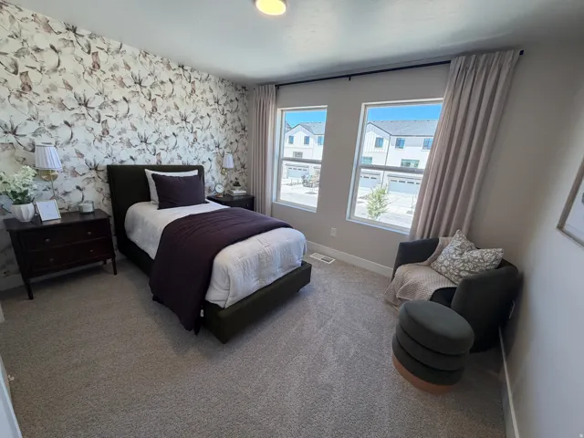Bedroom featuring a floral accent wall, two large windows with neutral curtains, and wall-to-wall carpeting