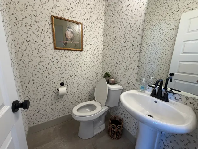 Powder room featuring a pedestal sink with matte black fixtures, botanical wallpaper, and durable flooring