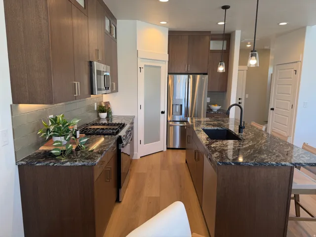 Gourmet kitchen featuring dark wood-finish cabinetry, stainless steel appliances, speckled stone countertops, and wood-finish flooring