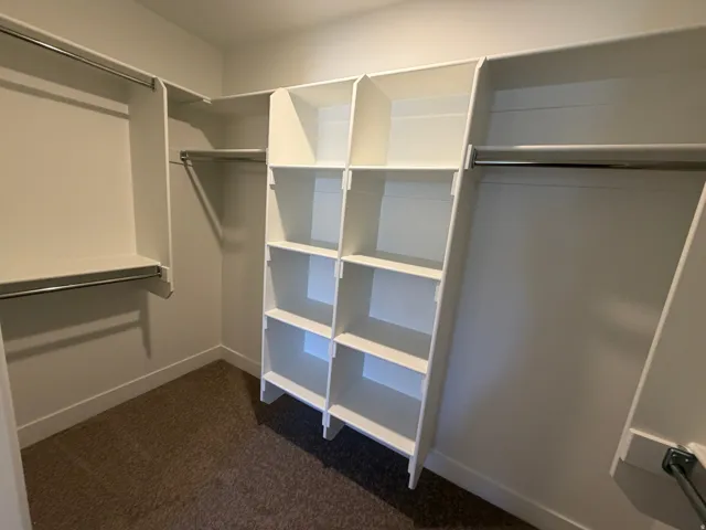 Walk-in closet featuring built-in white shelving, multiple hanging rods, and brown carpet flooring