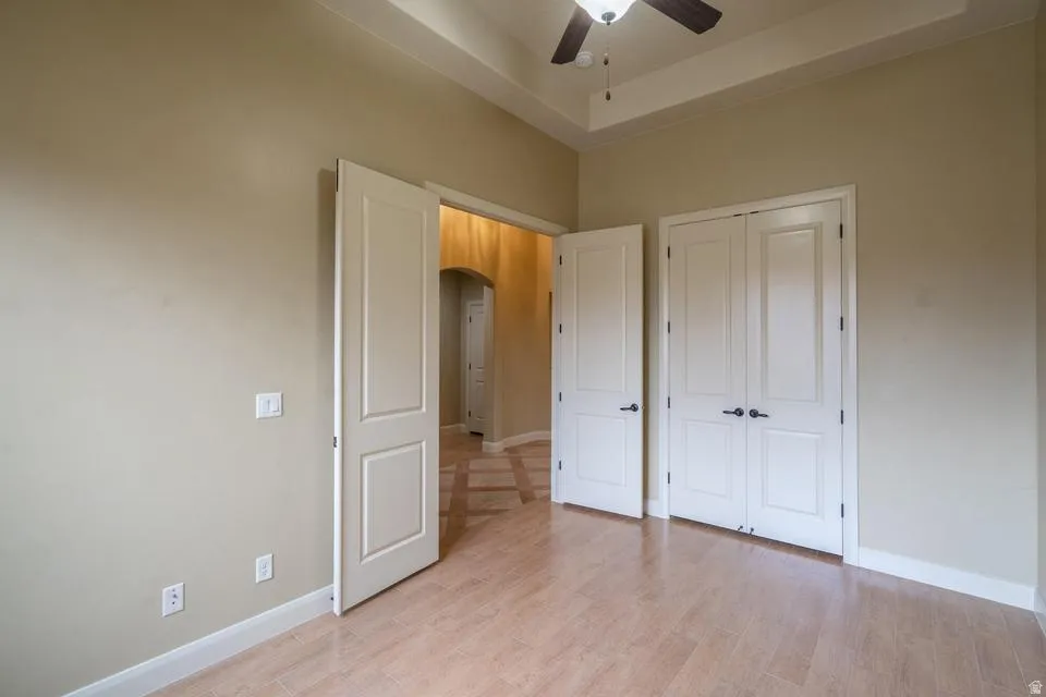 Tray ceiling with a ceiling fan, light wood-finish flooring, white baseboards, and panel doors with dark hardware