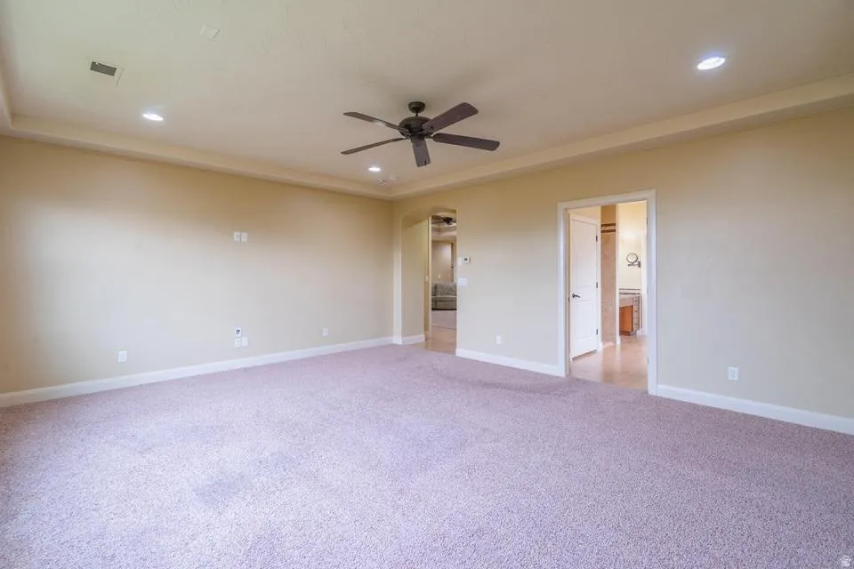 Spacious room featuring tray ceilings, recessed lighting, and a ceiling fan