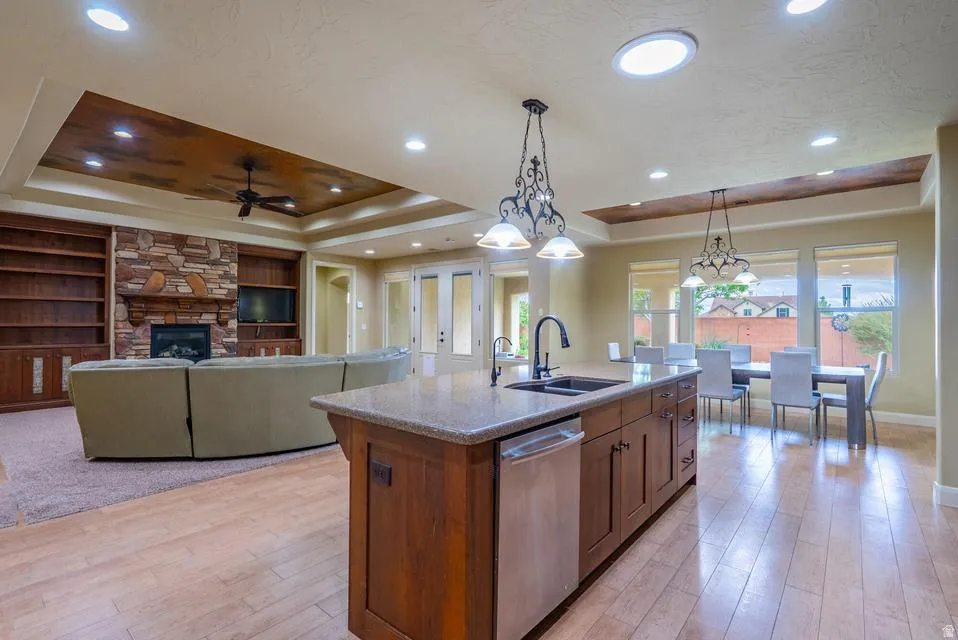 Open-concept living space featuring a central kitchen island with a stone countertop, a built-in stainless steel dishwasher, and a black faucet