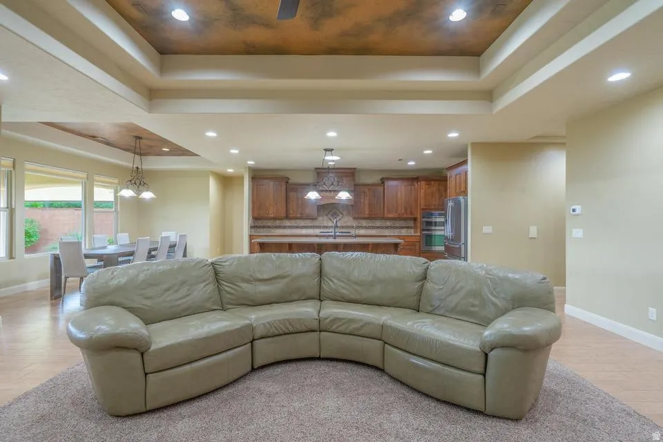 Open concept living area featuring a tray ceiling with recessed lighting, wood-finish flooring, and a kitchen with wood cabinetry and built-in appliances