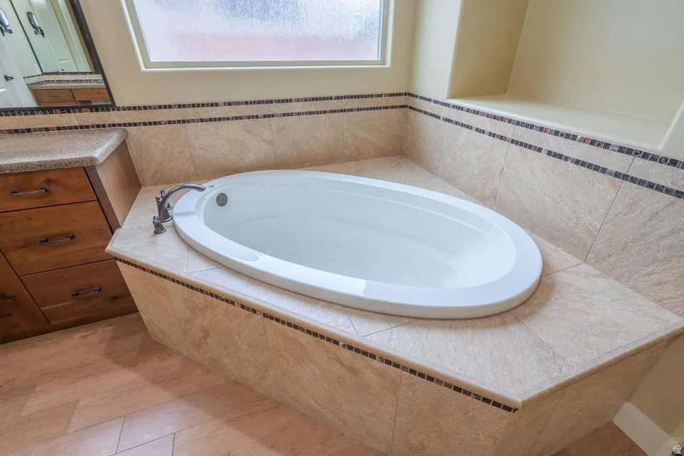 Recessed soaking tub with surrounding tilework, integrated window, and adjacent built-in cabinetry