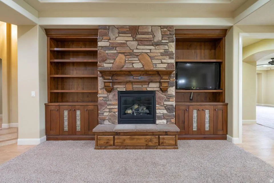 Stacked stone fireplace with gas insert, flanked by built-in shelving and cabinetry, featuring wood-finish construction and inset decorative panels