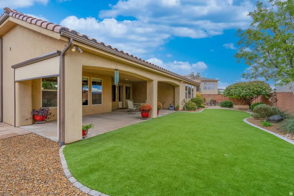 Expansive rear yard featuring an artificial turf lawn, a covered patio, and a gravel border