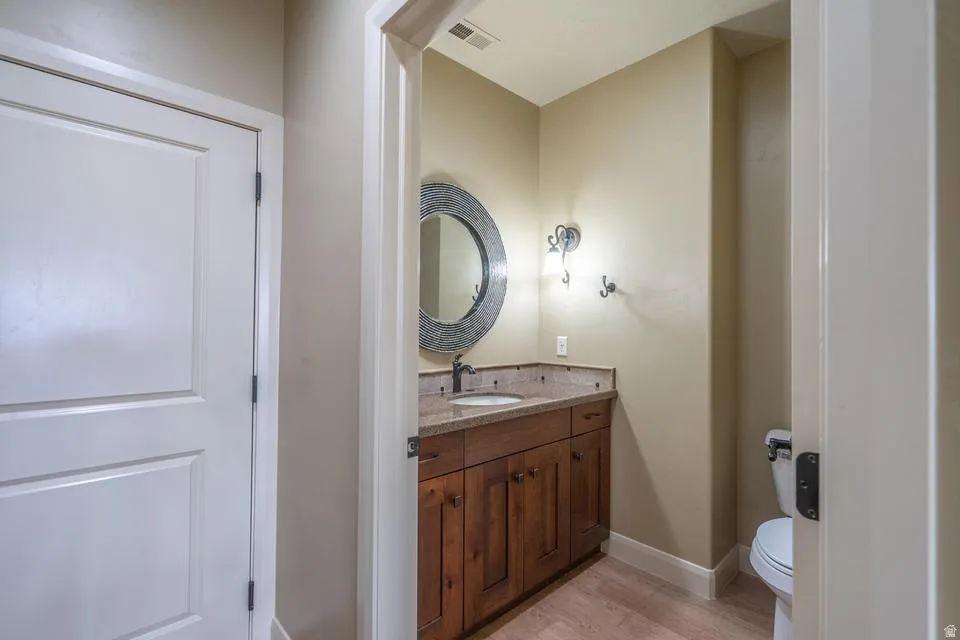 Powder room featuring a wood-finish vanity with an undermount sink, a stone-finish countertop, and a decorative round mirror