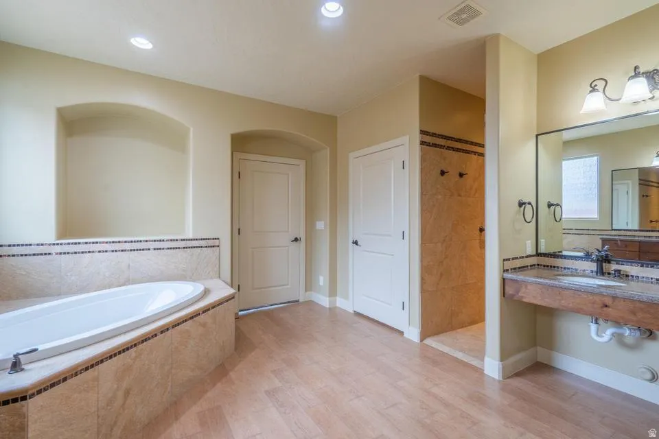 Spacious bathroom featuring a built-in soaking tub with tiled surround, a separate walk-in shower with tiled walls, and a vanity with an integrated sink and mirror