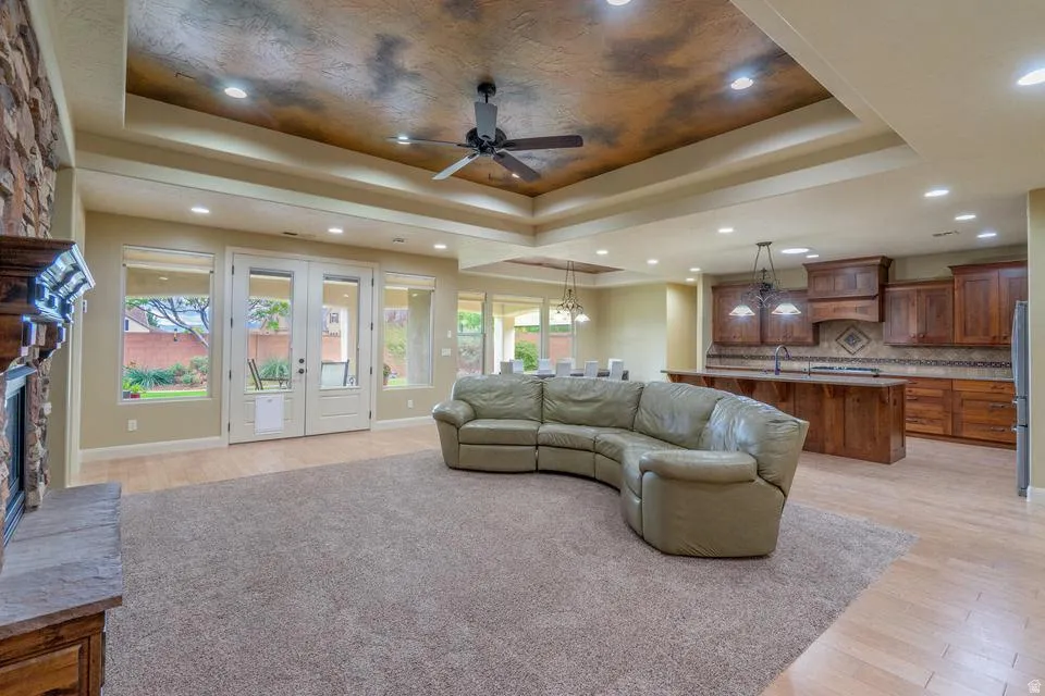 Spacious open-concept interior featuring a substantial area rug, wood-finish flooring, a tray ceiling with recessed lighting, and a ceiling fan
