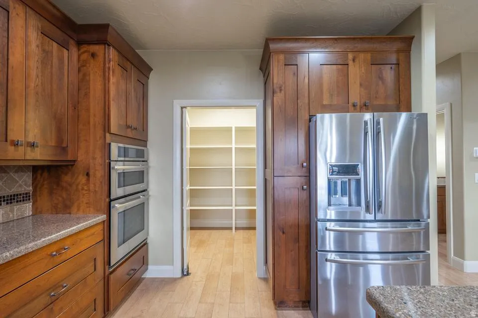 Kitchen featuring a stainless steel French door refrigerator, double wall ovens, rich wood cabinetry, granite-style countertops, and a tiled backsplash