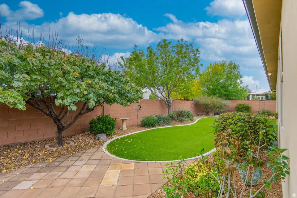 Enclosed backyard featuring artificial turf, mature trees, a low-maintenance gravel bed, and a block perimeter wall