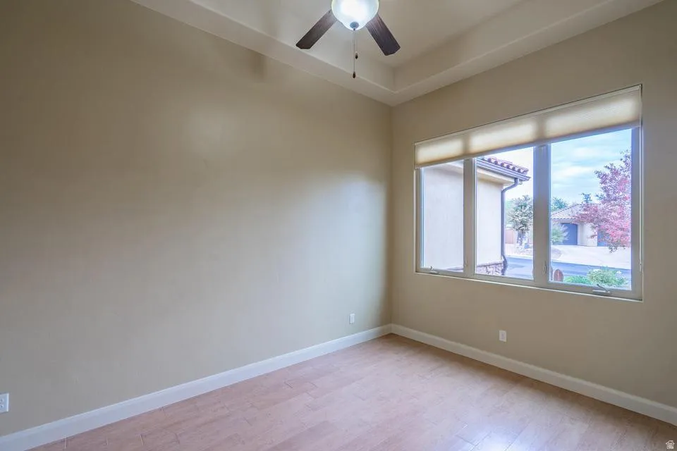 Room featuring a tray ceiling with a flush-mount ceiling fan, wood-finish flooring, and a large three-panel window with roller shades