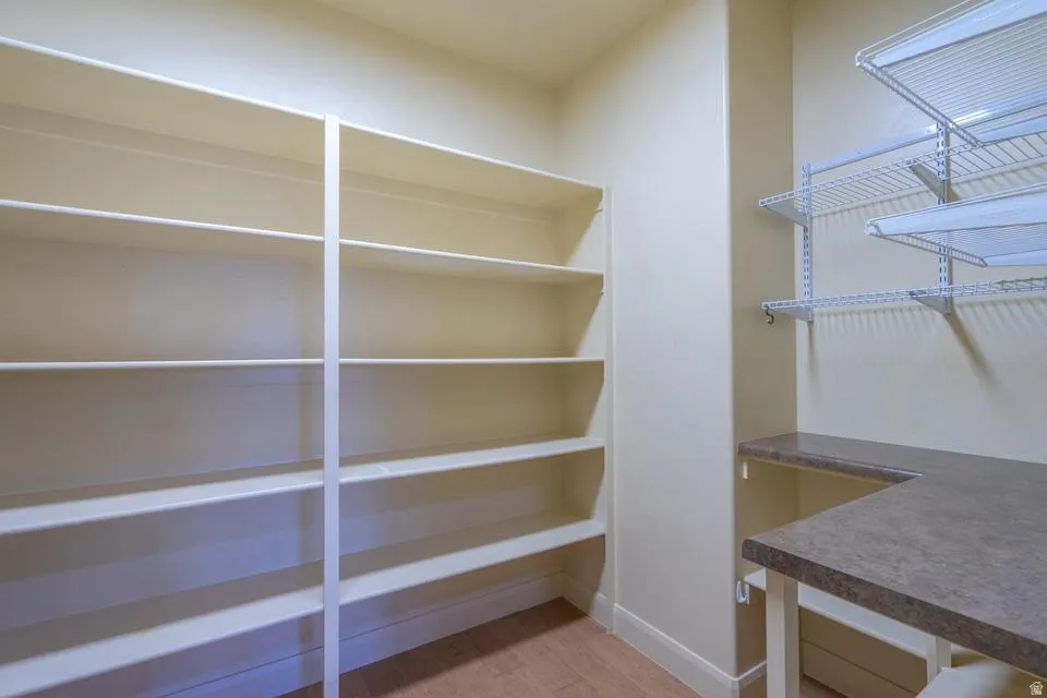Pantry featuring extensive built-in shelving, adjustable wire shelving, a U-shaped countertop, and wood-finish flooring