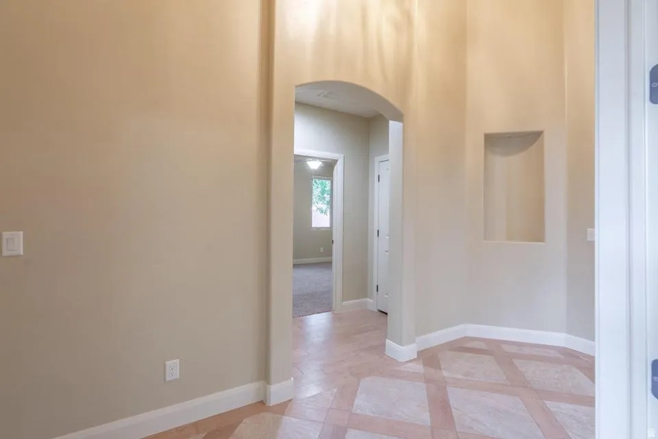 Tiled flooring with geometric pattern, arched entryway, recessed wall niche, neutral wall paint, and white baseboards