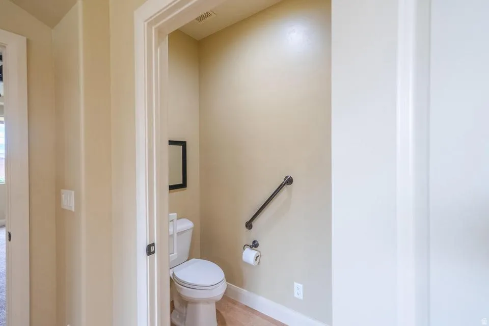 Compact water closet featuring a white toilet, black grab bar, and wood-finish flooring