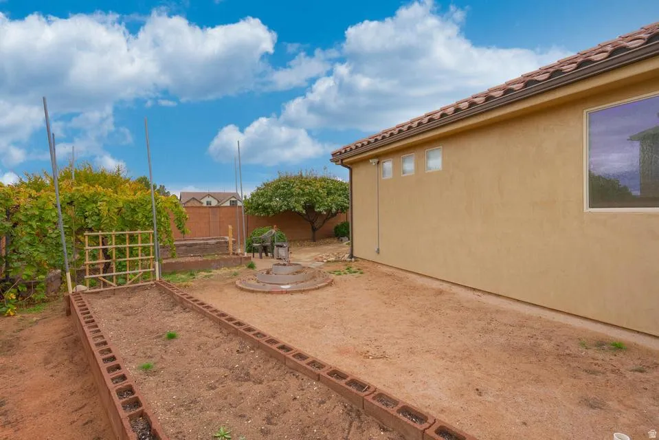 Expansive backyard featuring a stucco exterior with a tile roof, raised garden beds, and a circular stone planter