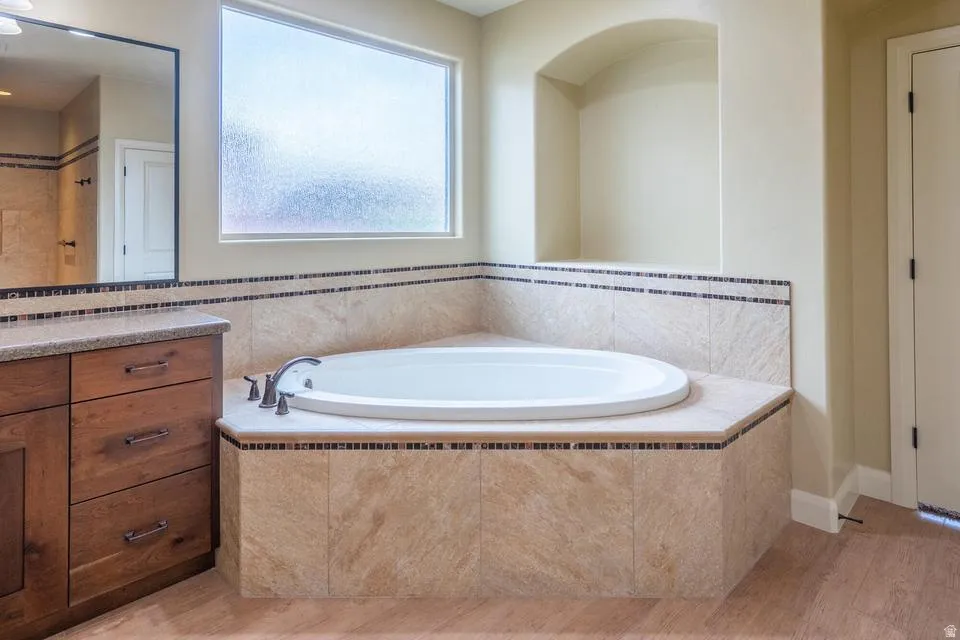 Built-in soaking tub with deck-mounted fixtures, surrounded by stone-look tile with mosaic accents