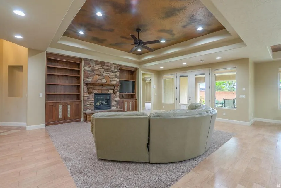 Spacious living area featuring a stone fireplace with a wood mantel, built-in shelving, a tray ceiling with recessed lighting and a ceiling fan, and light wood-finish flooring