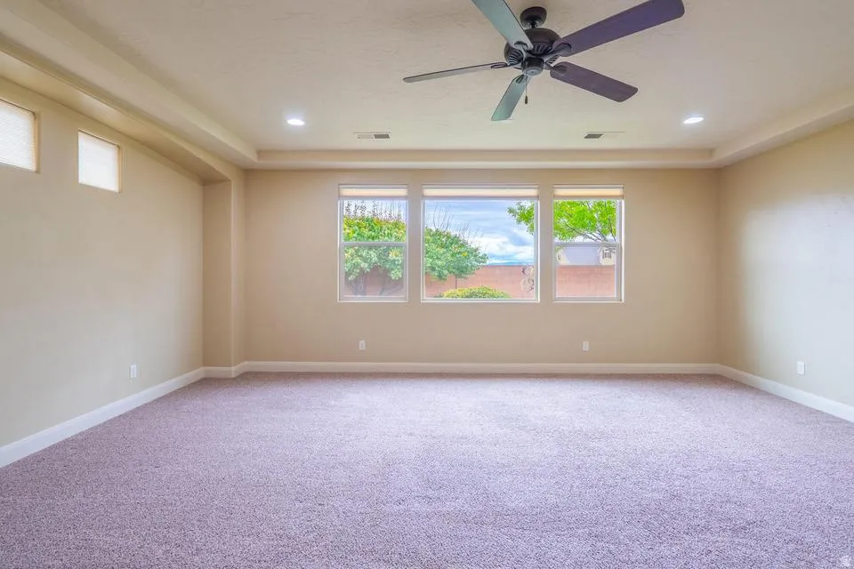 Spacious room featuring broadloom carpeting, a tray ceiling with recessed lighting, and a ceiling fan