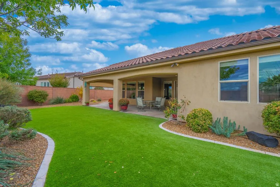 Expansive backyard featuring artificial turf, mature landscaping, and a covered patio