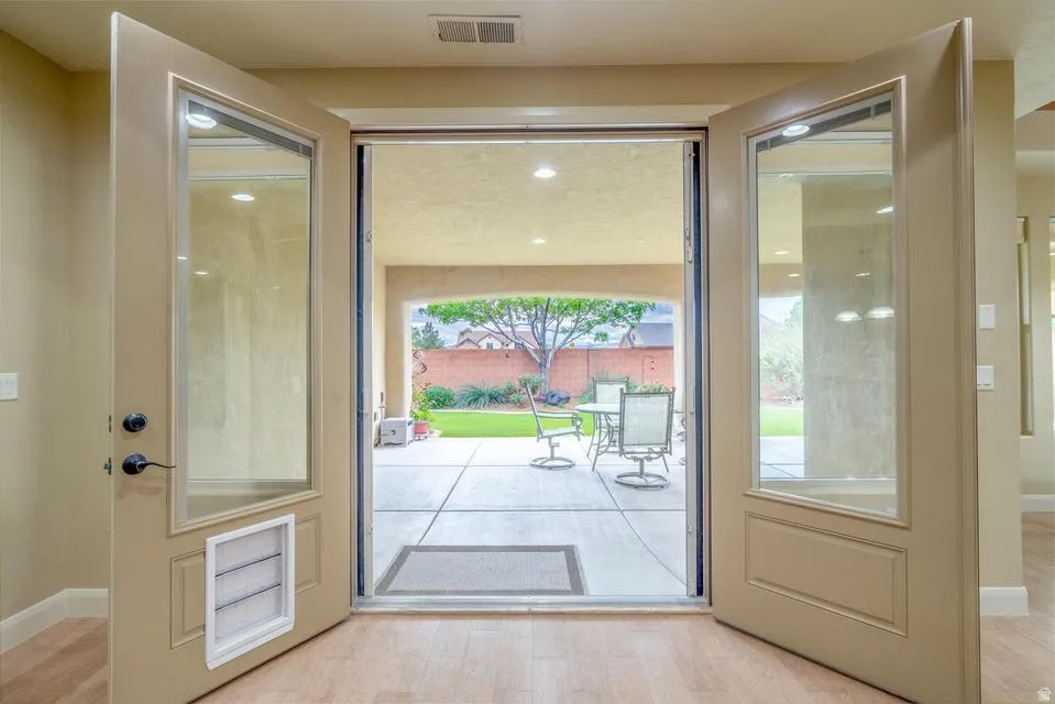 Double glass-panel doors open to an expansive backyard patio with concrete slab flooring and a manicured lawn