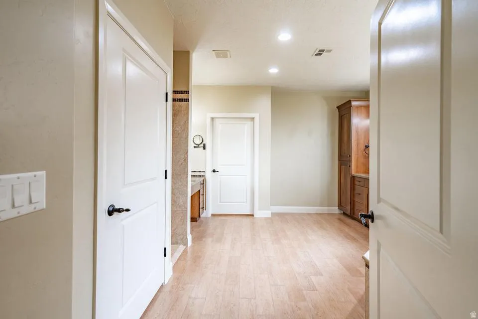 Spacious interior hallway featuring light wood-finish flooring, recessed lighting, and a built-in wood-finish cabinet with storage