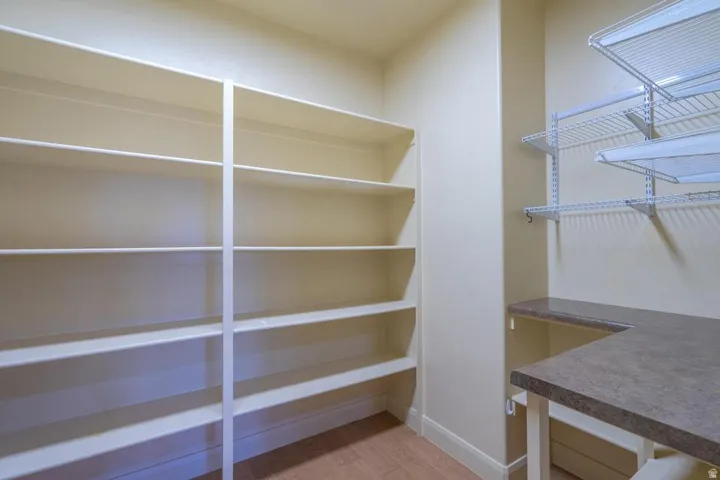 Pantry featuring extensive built-in shelving, adjustable wire shelving, a U-shaped countertop, and wood-finish flooring