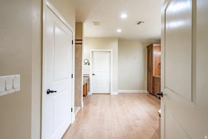Spacious interior hallway featuring light wood-finish flooring, recessed lighting, and a built-in wood-finish cabinet with storage