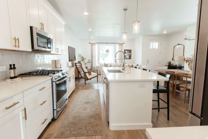 Open-concept kitchen featuring white cabinetry, stainless steel appliances, a subway tile backsplash, and a large island with an undermount sink