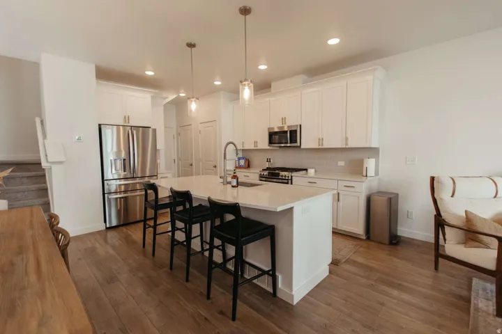 Kitchen featuring a large island with seating, stainless steel appliances, white cabinetry, light countertops, and wood-finish flooring