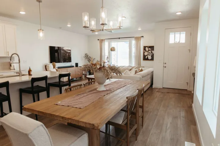 Open-concept living area featuring wood-finish flooring, a kitchen island with seating, pendant lighting, and a white paneled entry door with transom window