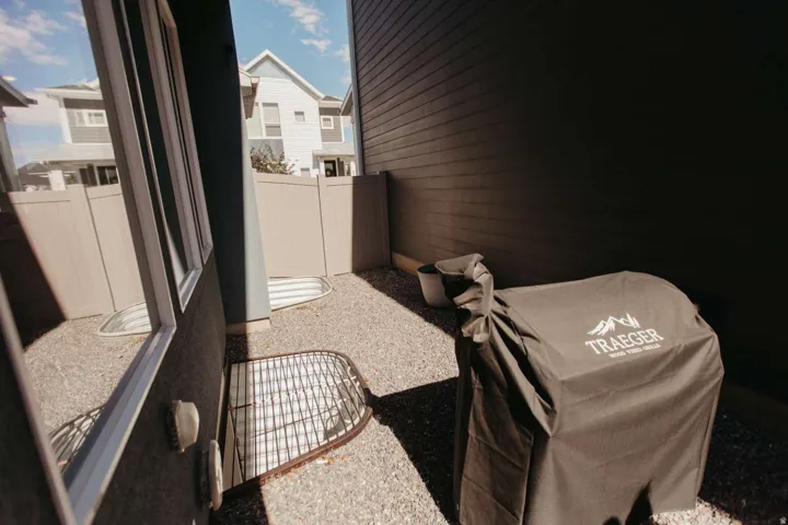 Private side yard featuring a gravel surface, secure fencing, and a window well with a protective grate