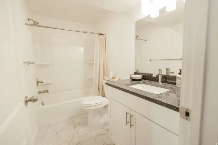 Bathroom featuring a white vanity with brushed nickel hardware, a dark speckled countertop, an undermount sink, and a mirrored wall