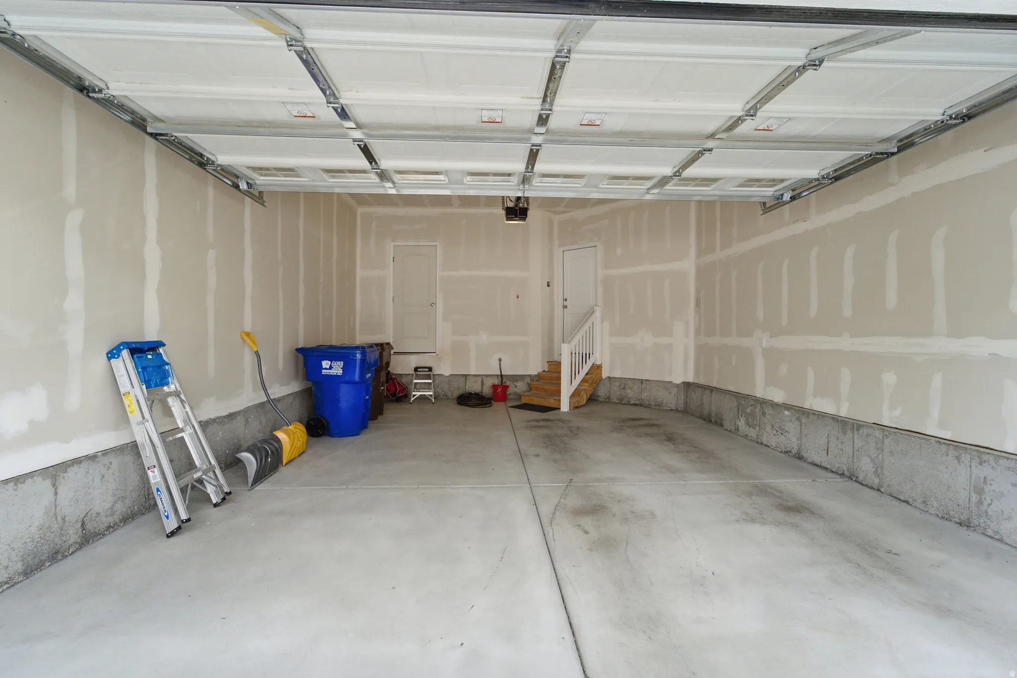 Spacious garage featuring a concrete floor, high ceilings, and access door. Other door is storage closet