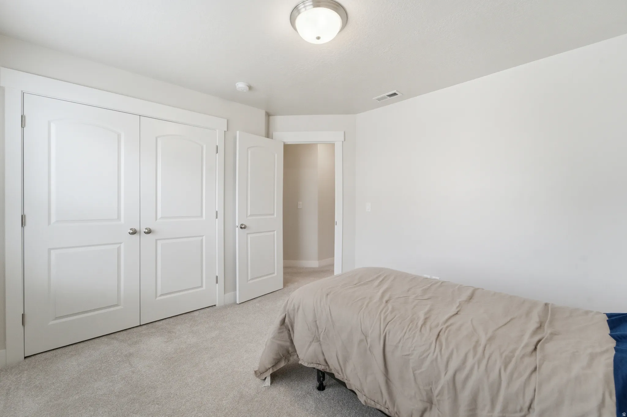 Light gray carpeting throughout a room featuring a double-door closet with paneled doors and brushed nickel hardware