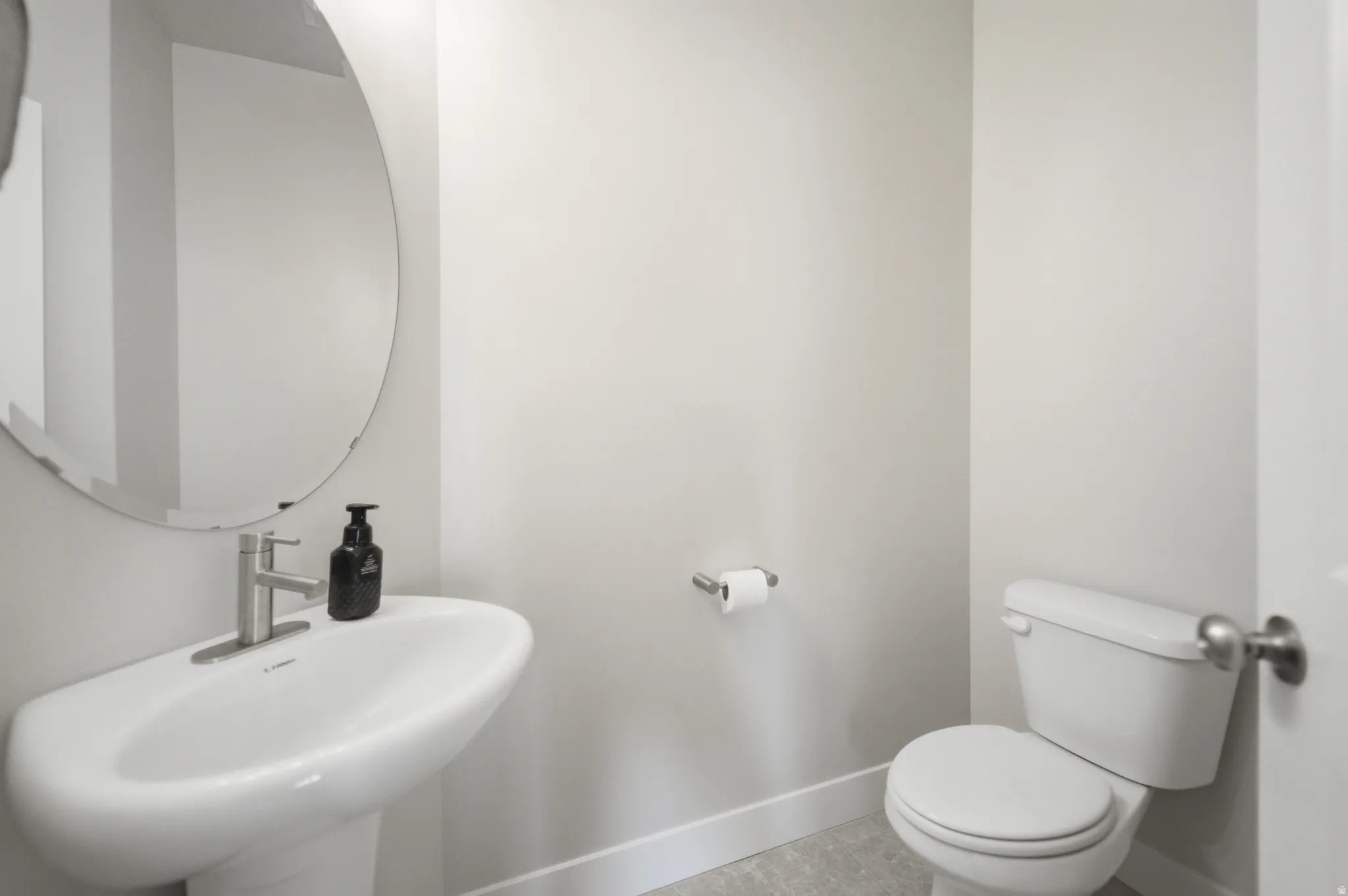 Pedestal sink with a brushed nickel faucet, round mirror, and a white toilet