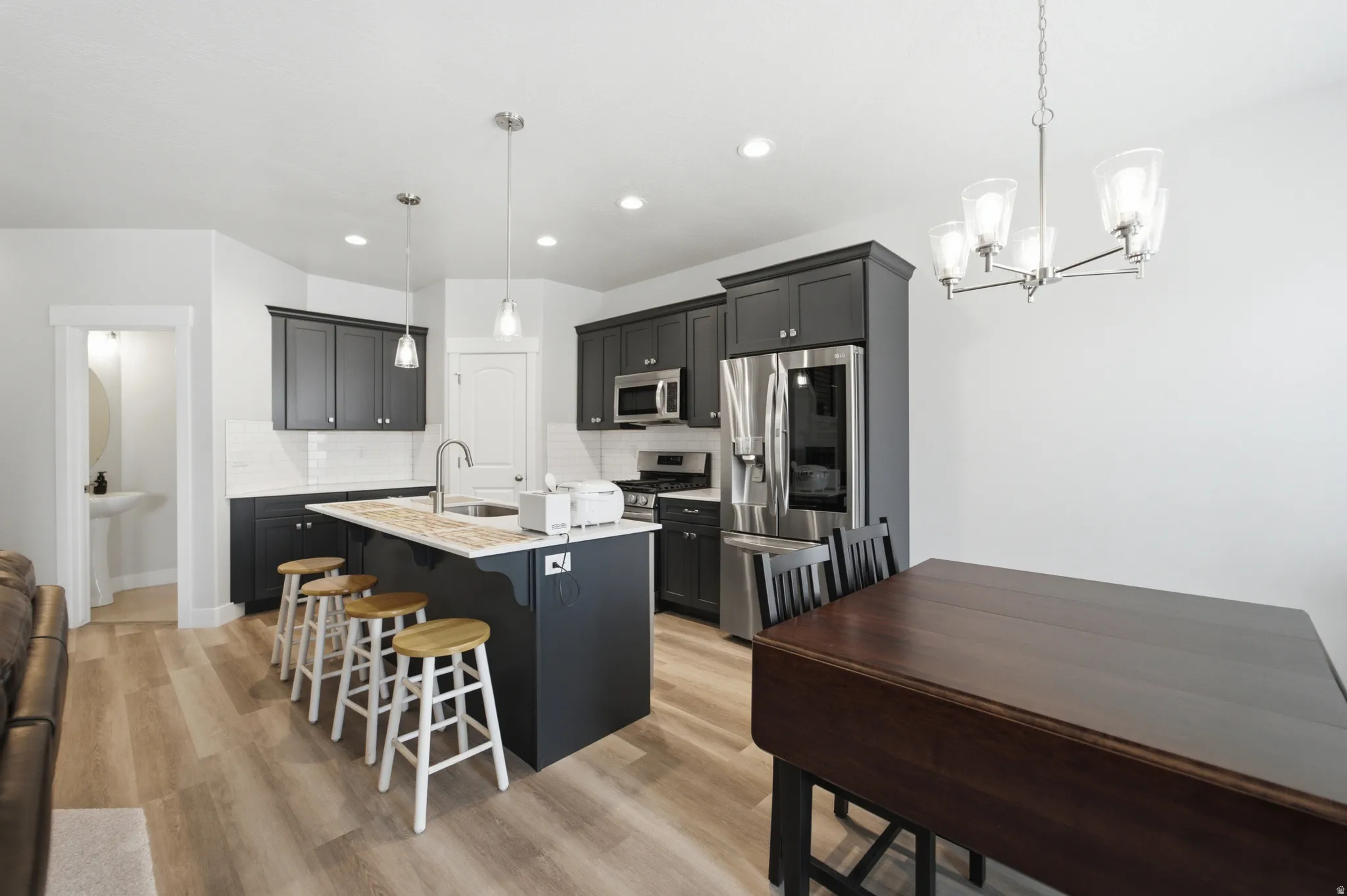 Open-concept kitchen featuring dark cabinetry, stainless steel appliances, a center island with pendant lighting, and wood-finish flooring