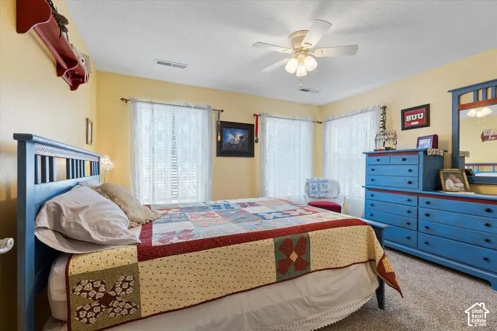Bedroom featuring neutral wall paint, carpet flooring, a ceiling fan with integrated lighting, and multiple windows with blinds
