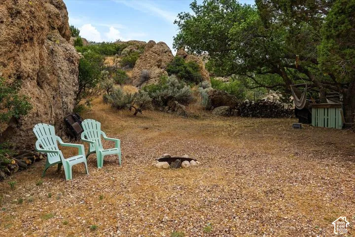 Outdoor gathering area featuring a stone-lined fire pit, natural rock formations, mature trees, and a gravel ground cover